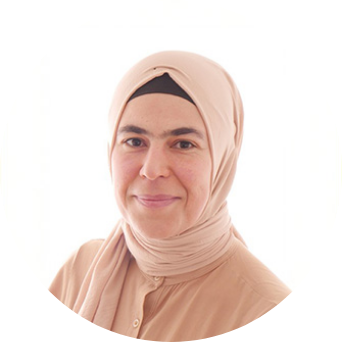 Porträt einer Person mit hellem Kopftuch und beigem Oberteil, die ruhig in die Kamera blickt. Der Hintergrund ist hell und schlicht.