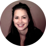 Porträt einer Person mit dunklem Haar, die freundlich lächelt. Der Hintergrund ist dunkel und leicht unscharf.