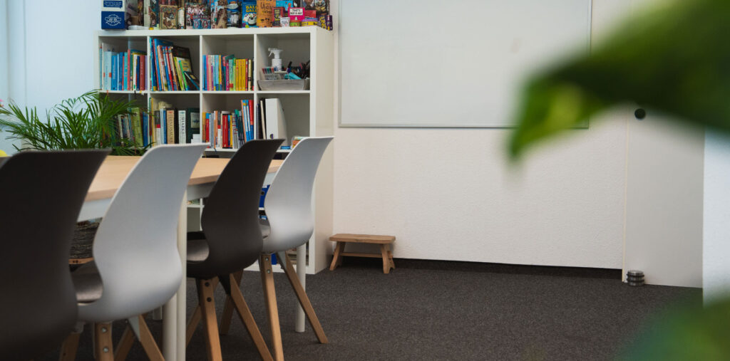 Arbeits- oder Gruppenraum mit Tisch, Stühlen, Bücherregal und Whiteboard an der Wand.