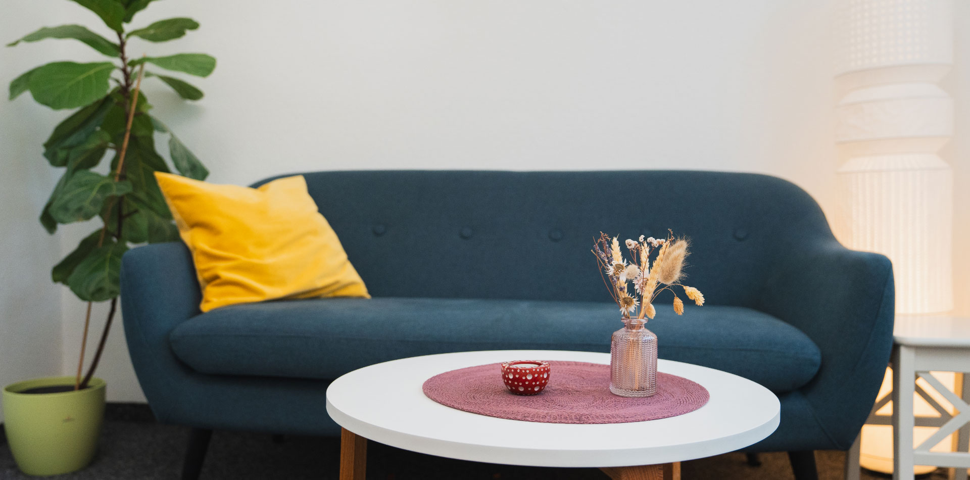 Gemütlicher Raum mit Sofa, rundem Tisch, Dekoration, Pflanze und Stehlampe.